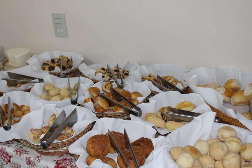 Cestas de pães, brioches e biscoitos artesanais dispostos sobre toalha branca em ambiente do sacramento palace hotel