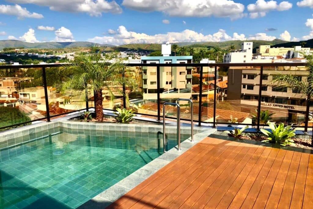 Piscina do hotel serravita cercada por plantas no terraço com vista para edifícios em paisagem urbana com montanhas. Ilustra onde ficar na serra da canastra