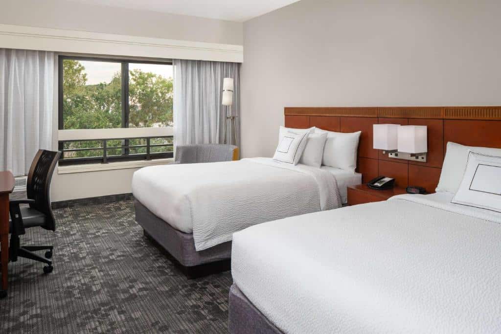 Quarto do Sonesta Select Miami Lakes com duas camas de casal, escrivaninha e janela com vista para área externa arborizada. Essa é uma das dicas de onde ficar perto do Hard Rock Stadium.