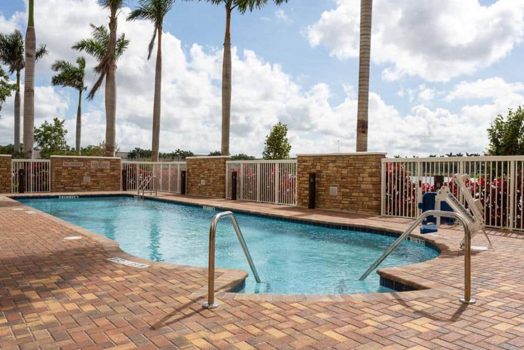 Piscina com deck de tijolinhos no SpringHill Suites by Marriott Fort Lauderdale Miramar com palmeiras altas ao fundo
