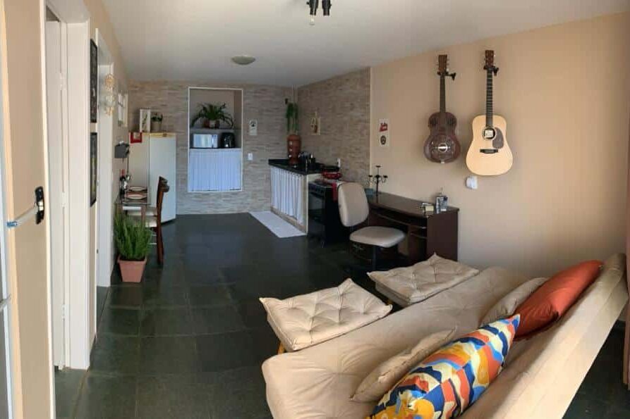 Sala de estar aconchegante no Studio do Wander com móveis de madeira, guitarra e violão pendurados na parede, além de um computador sobre a mesa.
