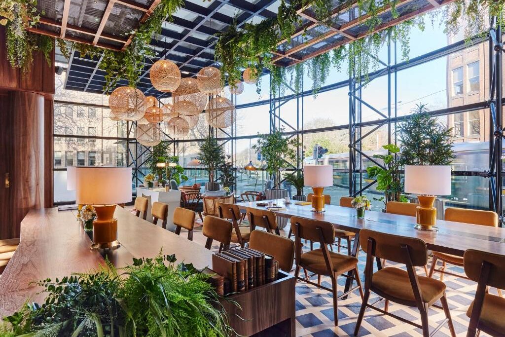 Salão de jantar no The Green com plantas pendentes, iluminação de design e cadeiras de madeira em cenário elegante