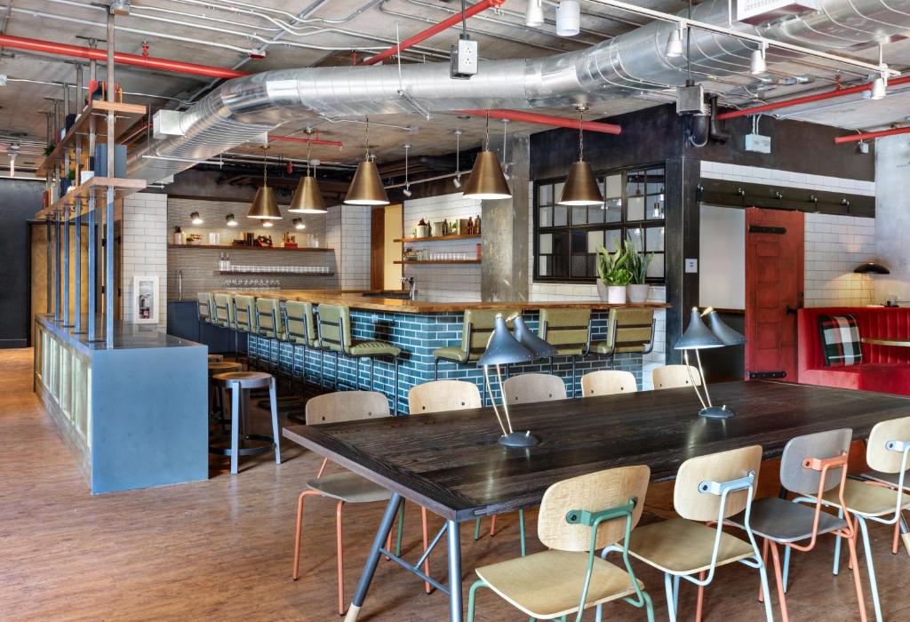 Ambiente de trabalho moderno do The Revolution Hotel com bancada de madeira, iluminação pendente elegante e paredes azul petróleo com tijolos à vista.
