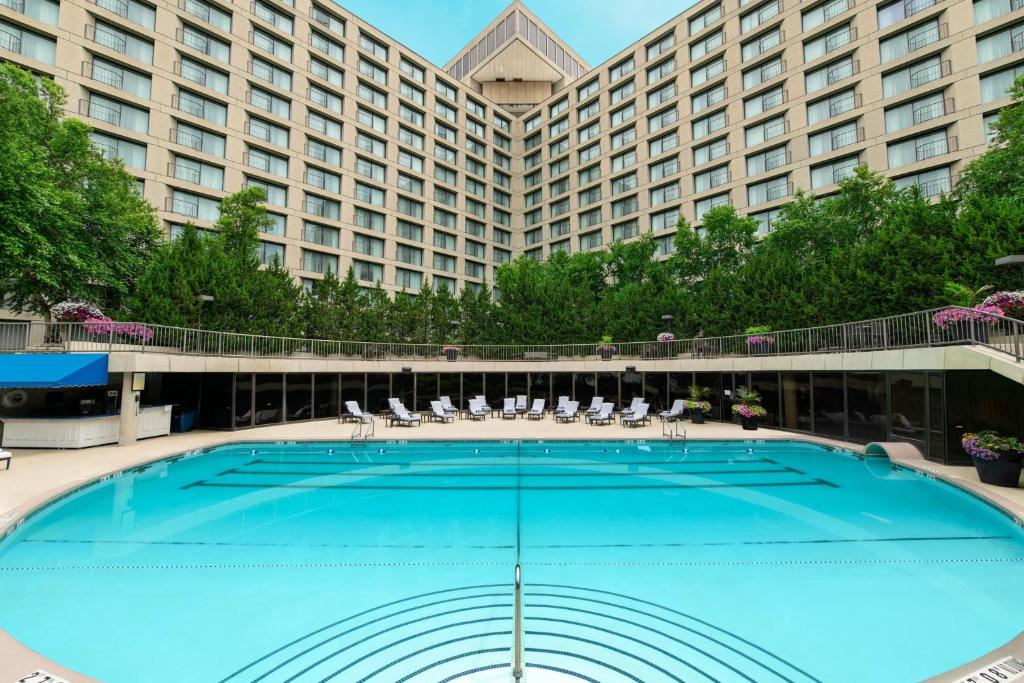 Piscina e centro de lazer no The Westin Kansas City at Crown Center com fachada moderna de vidro e madeira rodeada por vegetação verde.