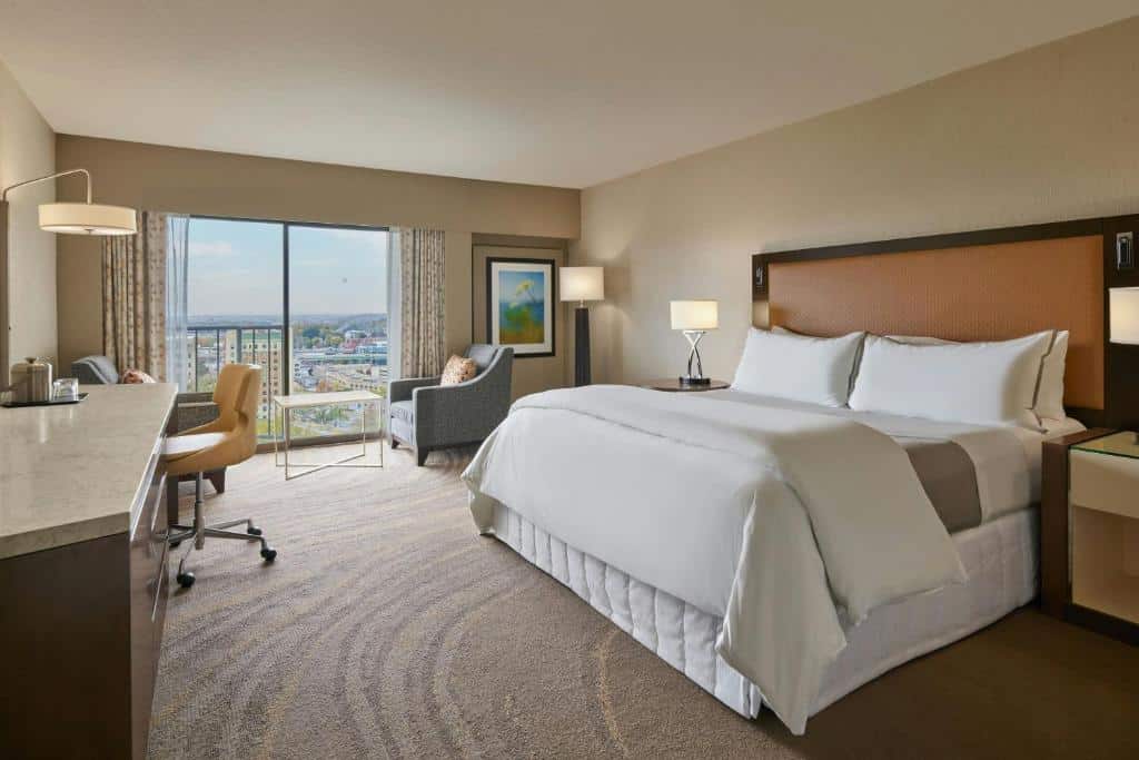 Quarto do The Westin Kansas City at Crown Center com vista panorâmica da cidade, cama king size, sofá cinza e mesa de trabalho com cadeira.