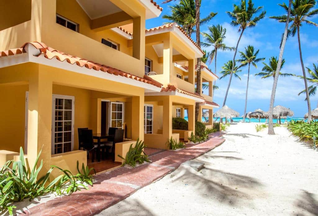Villas Chiara Punta Cana, casa de praia em Punta Cana com varandas, cercada por palmeiras em praia de areia branca e céu azul ensolarado.