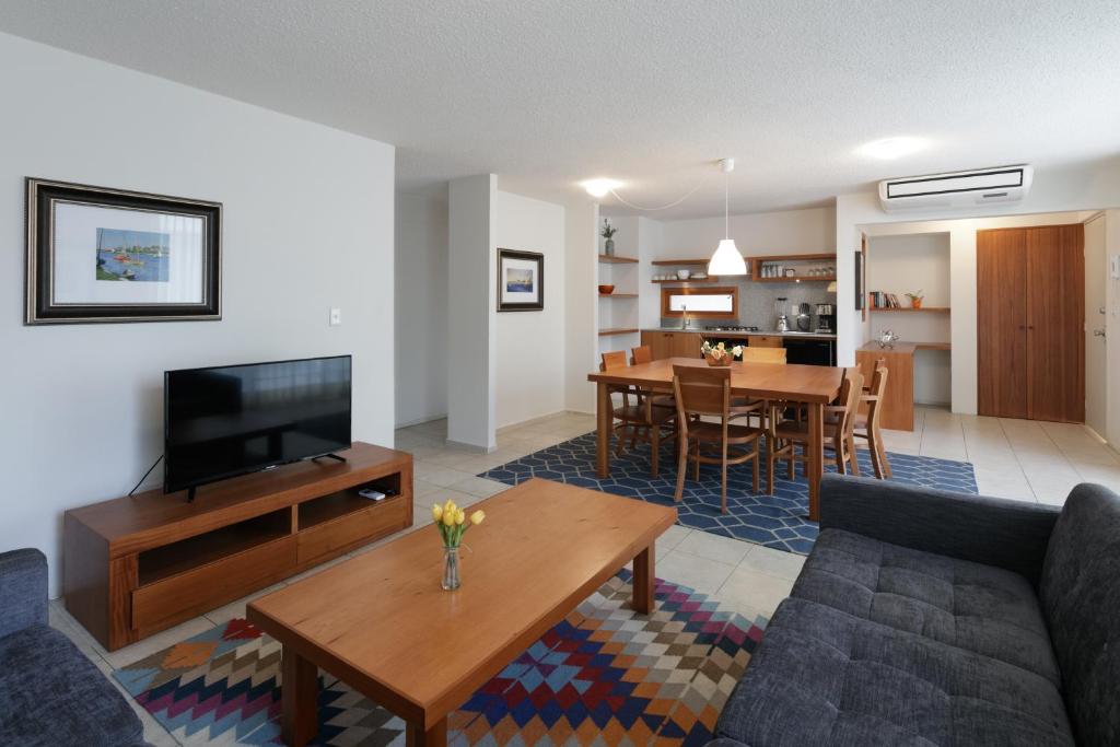 Sala de estar espaçosa com sofá cinza, TV em móvel de madeira, mesa de centro de madeira e cadeiras em torno de mesa de jantar em ambiente integrado à cozinha, no Apartamentos West End, para representar onde ficar em Guadalajara.