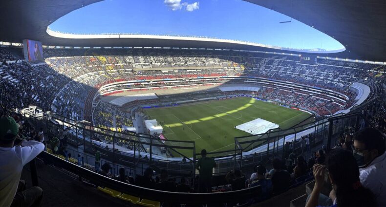 Estádio Azteca com milhares de torcedores assistindo a partida em um dia ensolarado. A imagem ilustra o post sobre onde ficar perto do Estádio Azteca.