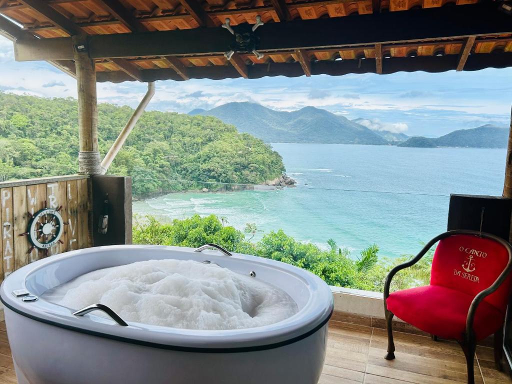 Jacuzzi redonda branca com hidromassagem em varanda de madeira com vista para praia e mata atlântica em Ubatuba. O local é a estadia Mirante do Pirata, localizad a na Praia Brava da Fortaleza