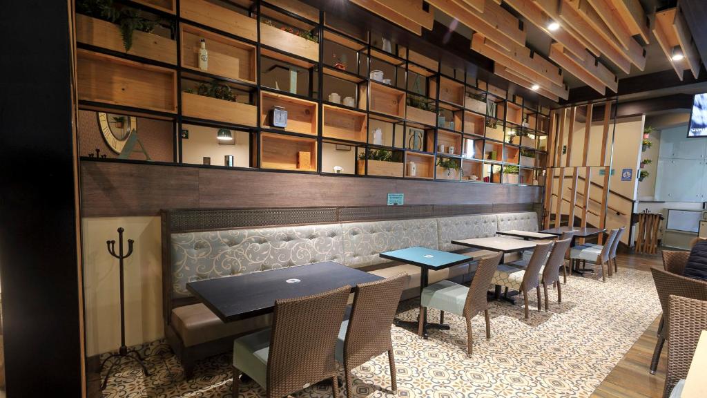 Espaço de restaurante do Holiday Inn Hotel & Suites Mexico Medica Sur by IHG com ampla estante de madeira exibindo diversos objetos decorativos, mesas e cadeiras de vime em ambiente aconchegante e moderno.