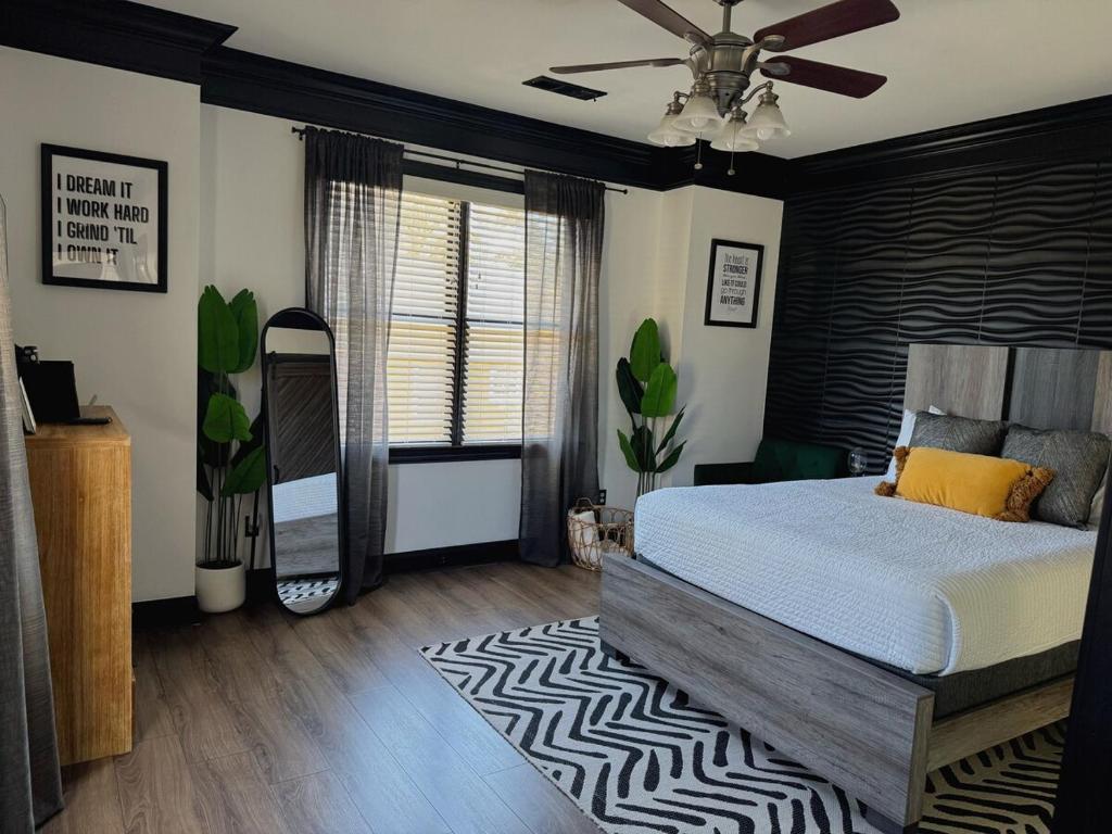 Quarto moderno do Vine City Bee Hive com decoração em tons de cinza, preto e verde, contendo cama com colcha azul, espelho, vasos de plantas e placa de parede com frase motivacional.