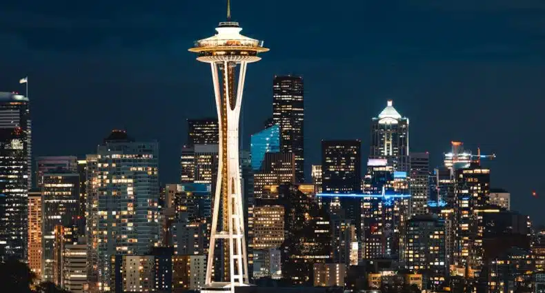 Space Needle, grande torre em Seattle iluminada à noite com o horizonte urbano da cidade ao fundo. A foto é capa do post de o que fazer em Seattle.