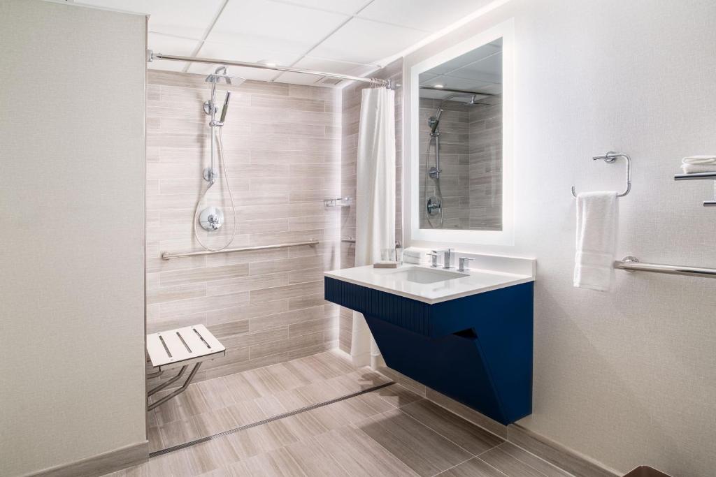 Banheiro moderno do the westin oaks com paredes revestidas em tonalidades claras, lavatório azul marinho, espelho e ducha embutida na parede.