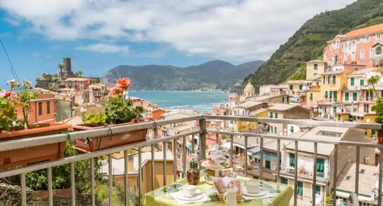 Vista panorâmica da Casa Catò de Vernazza, vila pitoresca da região italiana de Cinque Terre, com suas casas coloridas, ruas estreitas e barcos no porto. A imagem ilustra o post sobre onde ficar em Cinque Terre.