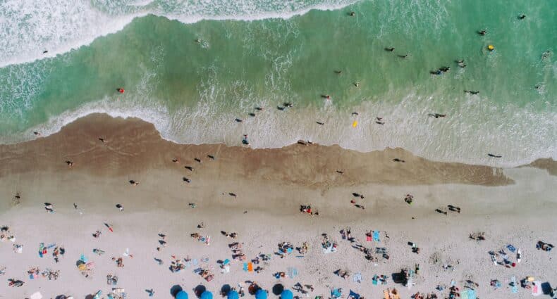 Dezenas de pessoas relaxando e se divertindo na praia com ondas verdes suaves e céu azul de Cocoa Beach, nos Estados Unidos
