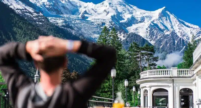 Imponentes montanhas nevadas com pinheiros verdes em primeiro plano, em cenário do La Folie Douce Hotels Chamonix de esqui com varanda e arquitetura clássica. A imagem ilustra o post sobre onde ficar em Chamonix.