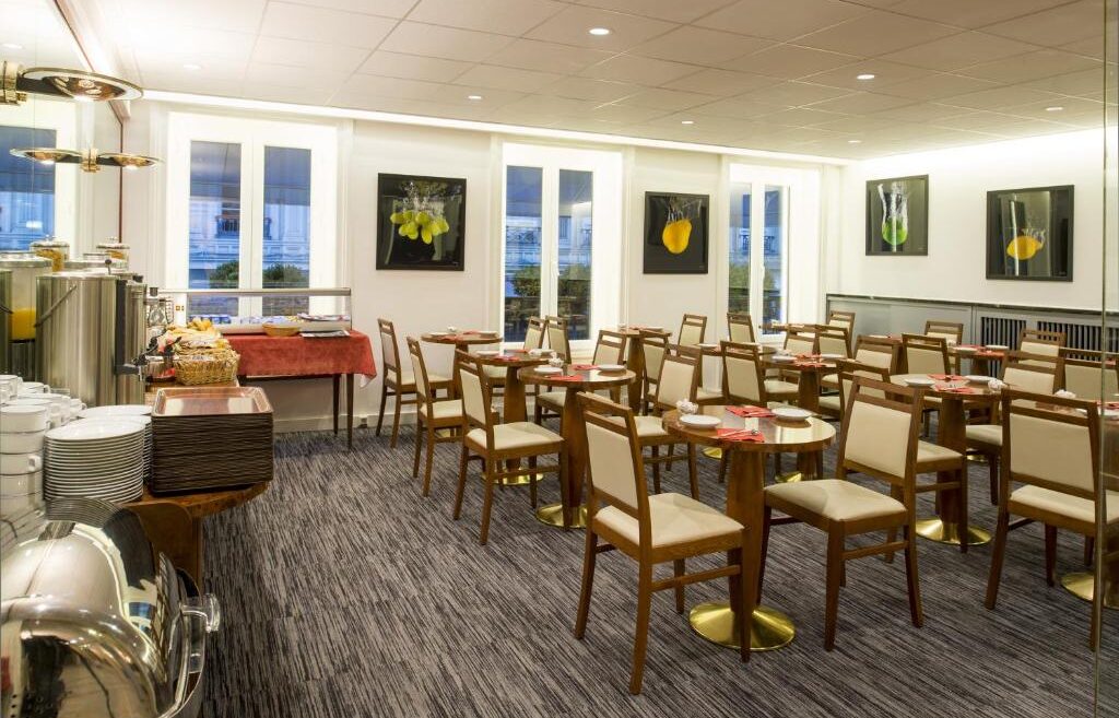 Salão de café da manhã no La Résidence com buffet variado, mesas e cadeiras confortáveis. Essa é uma das dicas de onde ficar em Lyon.