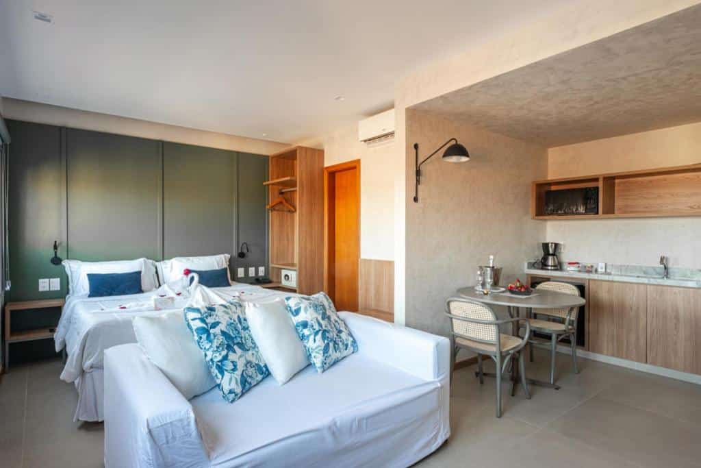 Quarto de hotel com parede verde, cama de casal com roupa de cama florida, mesa de jantar com cadeiras, armários de madeira, ar-condicionado e iluminação embutida no teto.

Ilustra os hotéis perto do Aeroporto de Salvador.