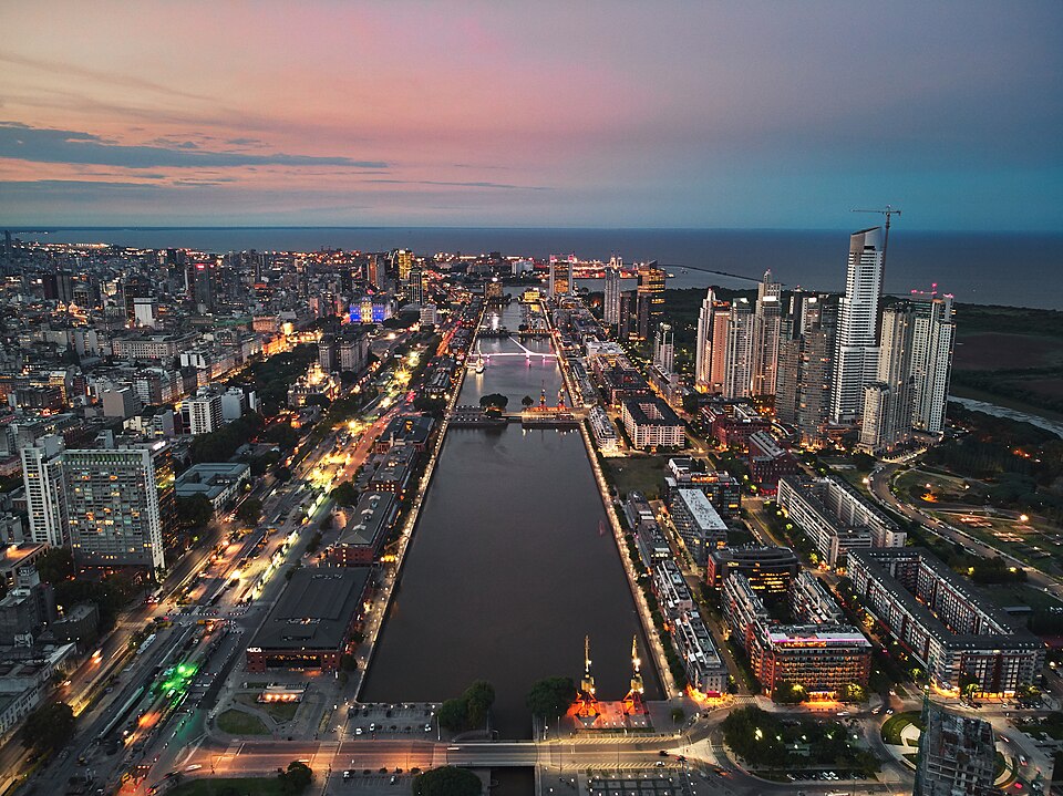 Vista aérea noturna do cais de Puerto Madero, em Buenos Aires, com prédios iluminados e céu alaranjado