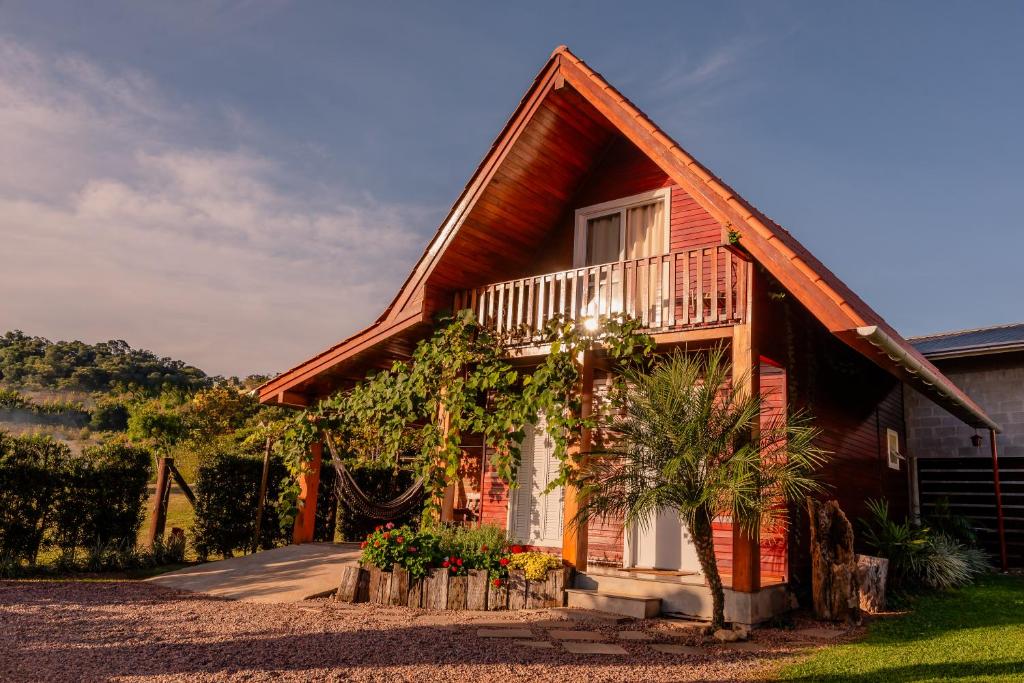 Chalé de madeira rústico com varanda e jardim florido, ideal para aluguel de temporada em área rural. Ilustra os chalés em Bento Gonçalves.