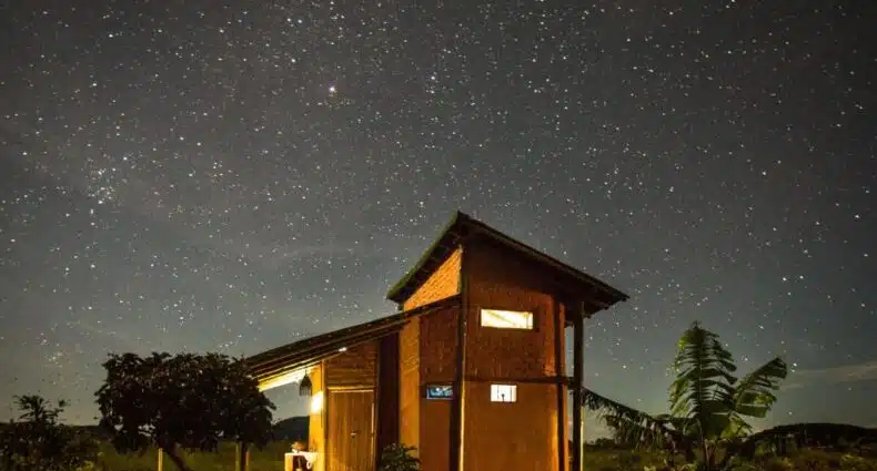 Casa de campo iluminada sob céu estrelado com Via Láctea visível à noite