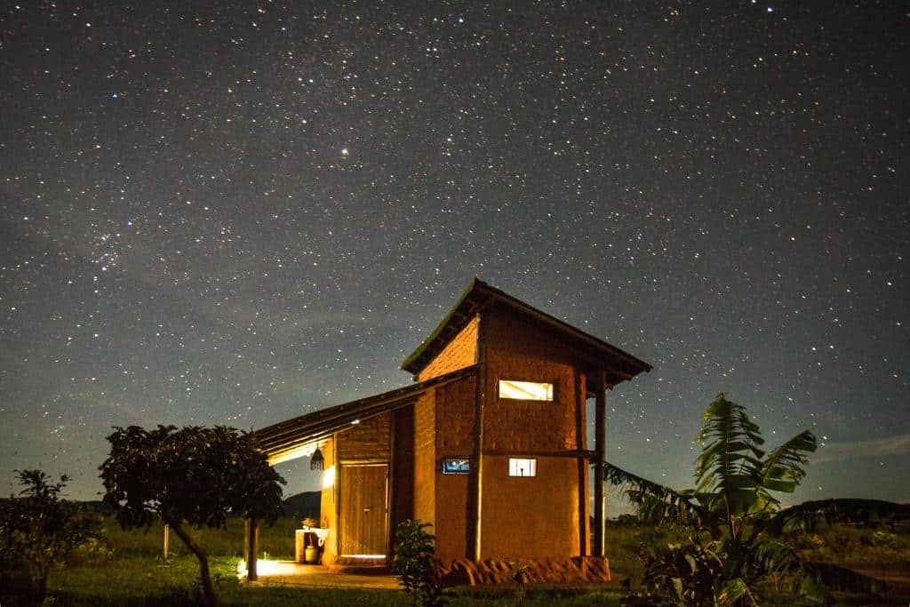 Casa de campo iluminada sob céu estrelado com Via Láctea visível à noite