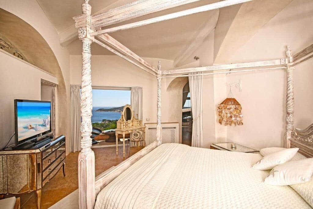 Quarto de hotel luxuoso com cama de dossel branca, vista para o mar e TV de tela plana