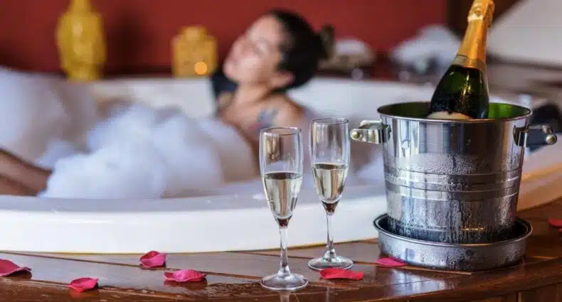 Banheira de hidromassagem com espuma, champanhe e taças para celebração romântica no Carícia do Vento Pousada Boutique. Representa chalés românticos em Monte Verde.