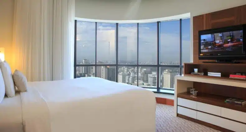 Quarto do luxuoso Renaissance São Paulo Hotel com vista panorâmica da cidade de São Paulo e cama de casal grande. Representa os hotéis perto da Avenida Paulista