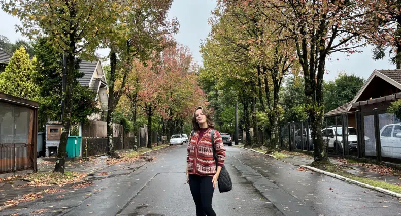 Mulher sorrindo em rua arborizada com árvores em tons de outono e casas em Gramado, Rio Grande do Sul