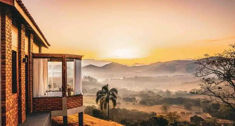 Casa de campo com vista para montanhas ao amanhecer, no Refúgio Terras Altas. Representa chalés no sudeste do Brasil.