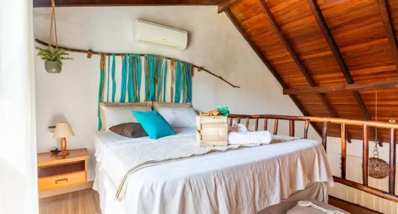 Quarto de casal aconchegante com cama de casal branca, ar condicionado e decoração rústica em madeira