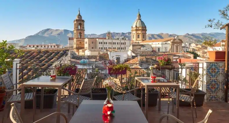 Terraço do La Terrazza sul Centro com vista para igrejas históricas e montanhas. Essa é uma das indicações de onde ficar em Palermo.
