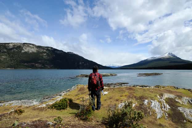 Homem de costas admirando paisagem com lago e montanhas nevadas na Patagônia