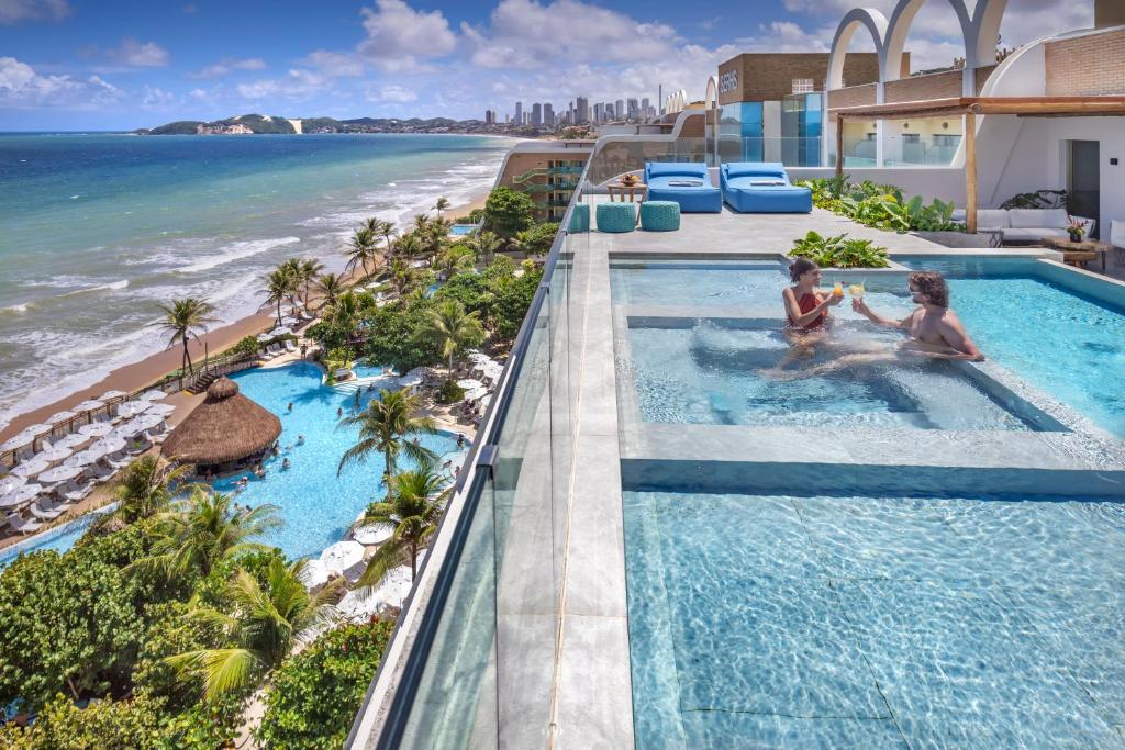 Casal brindando com drinks em piscina com borda infinita e vista para praia no Serhs Natal Grand Hotel & Resort. Representa melhores resorts para casais.