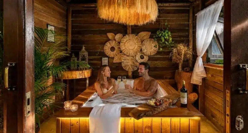 Casal relaxando em hidromassagem com champanhe e frutas em hidro num dos chalés românticos em Santa Catarina do Chalés Magia do Campeche.