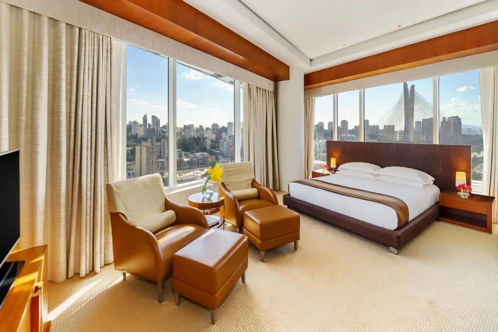 Quarto do Grand Hyatt com uma cama de casal, duas poltronas e vista panorâmica do skyline da cidade. A foto faz parte do post de Hotéis com ceia de Réveillon e Natal.