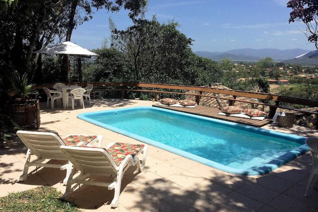 Piscina retangular azul em área de lazer com espreguiçadeiras e vista para montanhas no Studios do Barão. Essa é uma das indicações de chalés românticos em Santa Catarina.